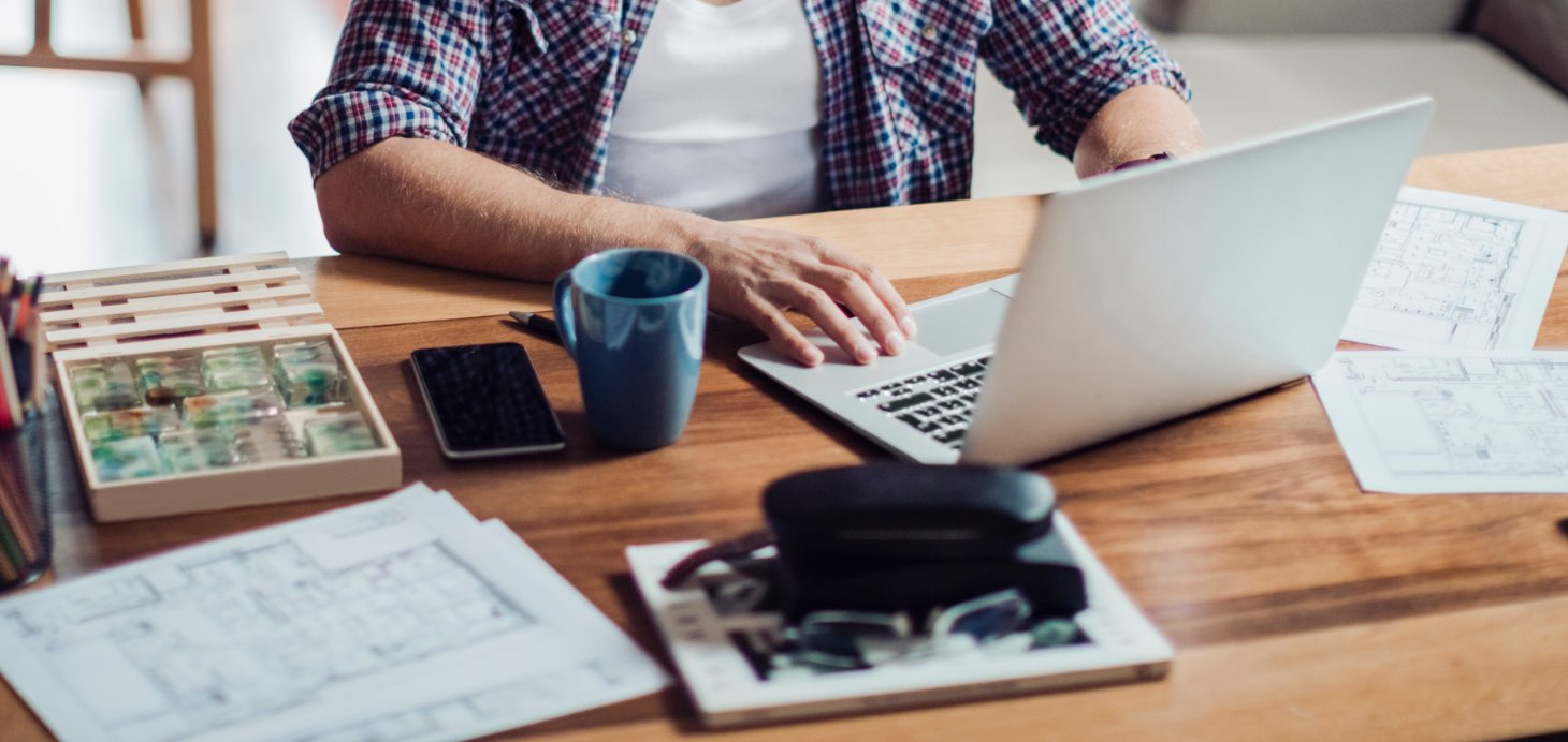 Schreibtisch mit Laptop und einem Mann mit einem Hemd im Hintergrund