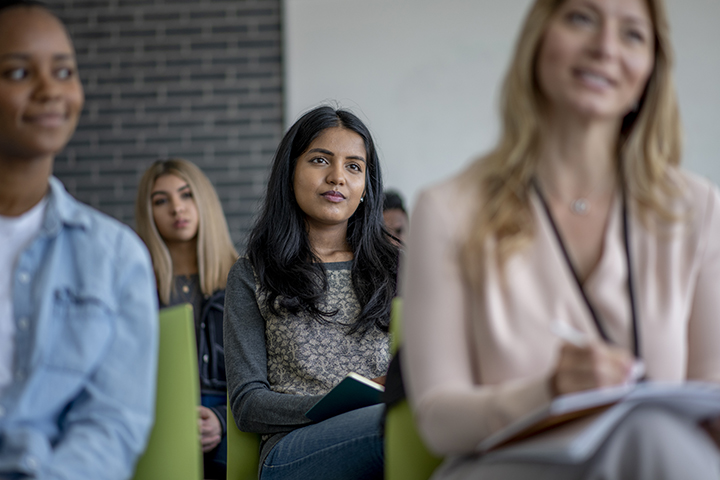 femme assise dans un public rempli de professionnels écoutant un orateur