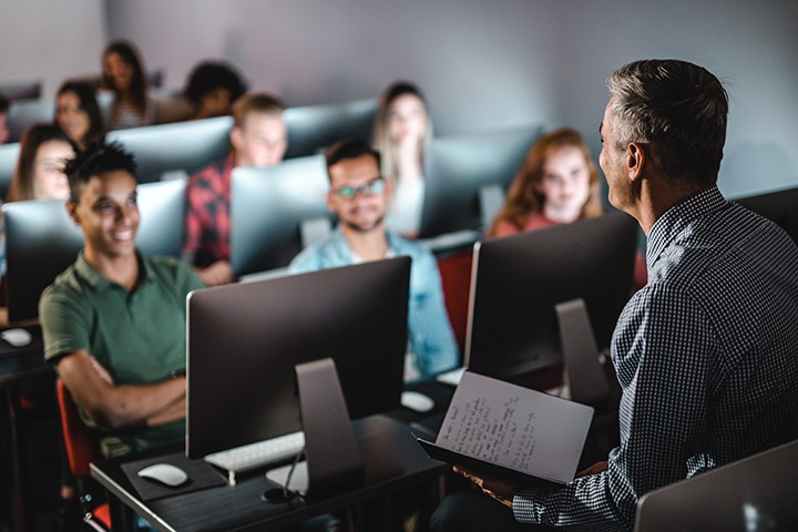 Teacher teaching in front of a group of students with laptops open