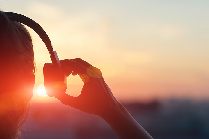 fille qui porte des ecouteurs et qui regarde le coucher du soleil