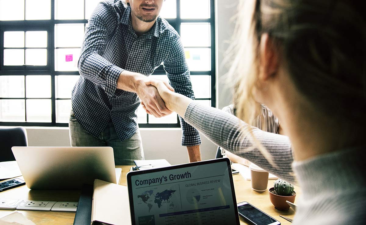 Two co-workers sitting across a table from each other shaking hands