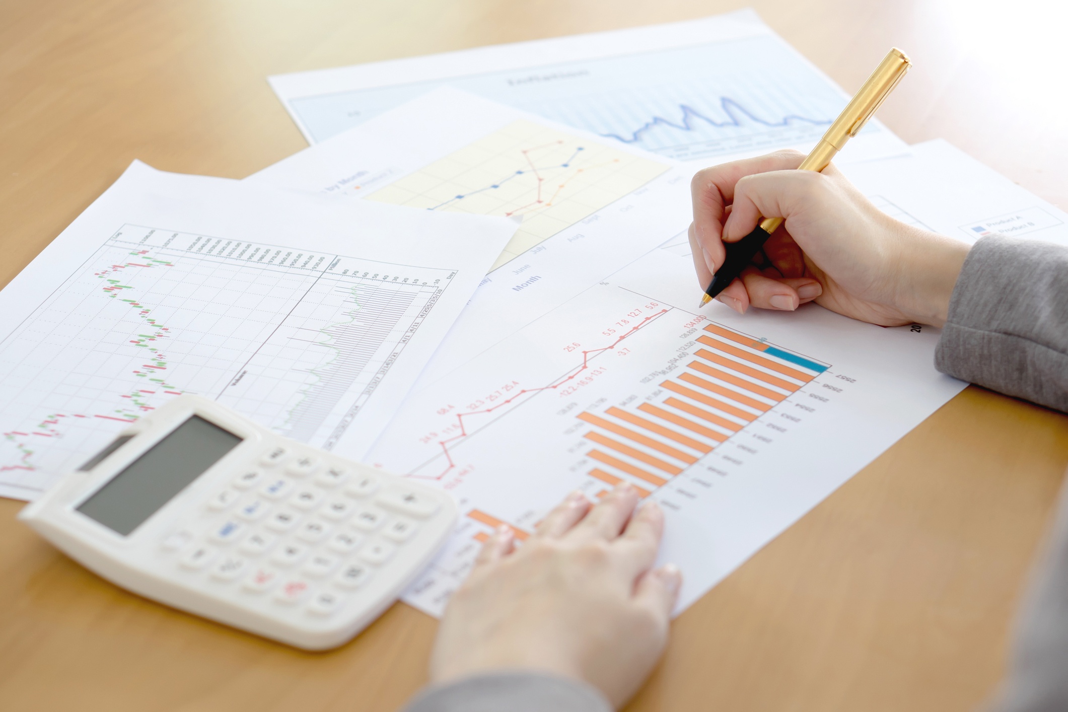 Pages of printed graphs spread out on a table with calculator and person writing with a pencil