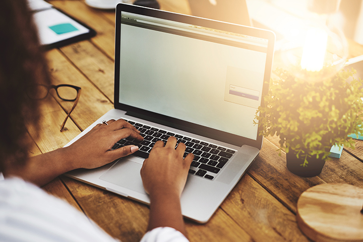 Cropped shot of a woman using her laptop on a wooden table