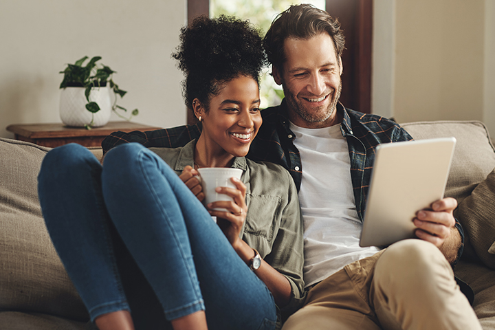 Shot of a happy young couple using a digital tablet together while relaxing on a couch at home