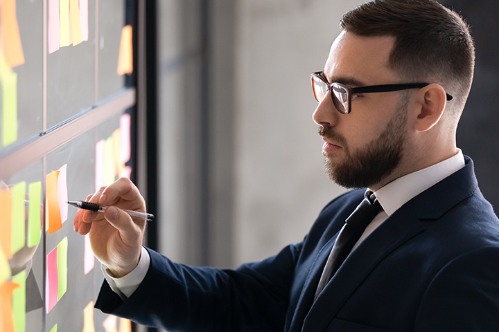 Mann mit Brille vor einer Pinnwand mit vielen Zetteln