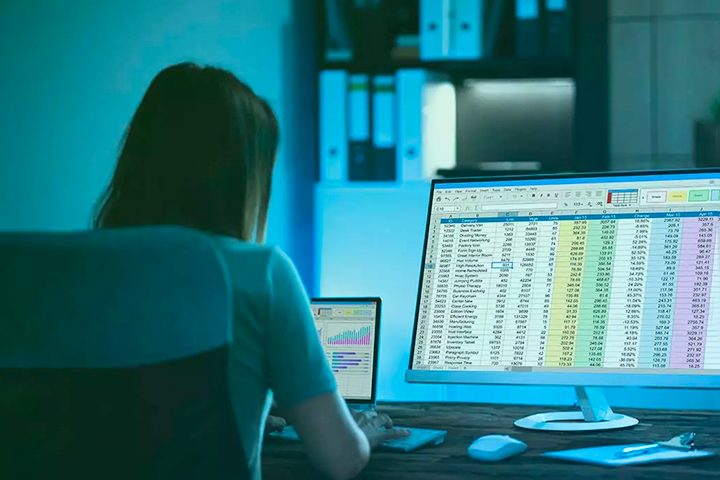 Woman in dark room looking at spreadsheets on computer screens