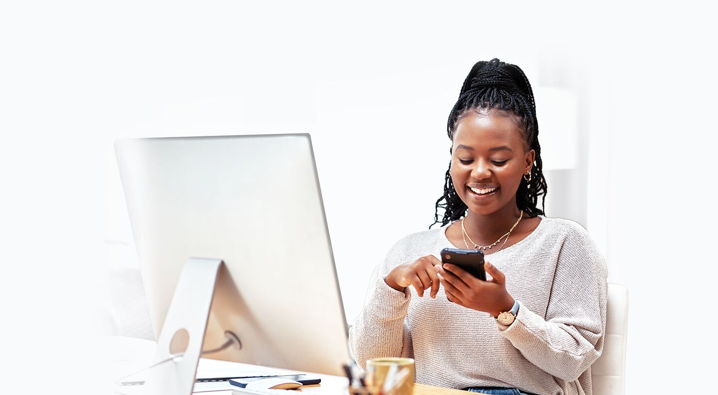 woman smiling looking at smartphone in front of a computer