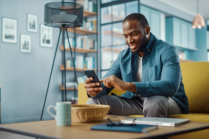 male customer holding mobile phone in his apartment at a coffee table