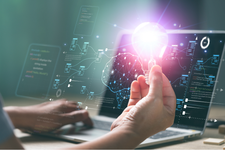 a person's hand holding a light bulb whilst using a laptop