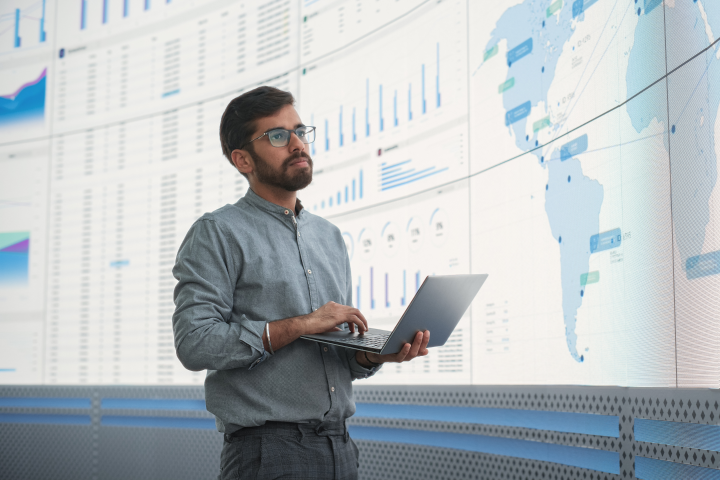 a man in front of a giant screen looking at world map and charts in light blue and white