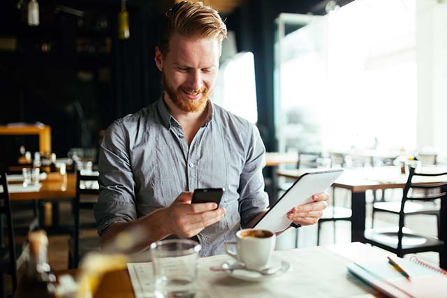 men holding a phone and tablet at a cafe