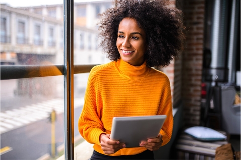 femme qui a sa tablette dans ses mains assie pres d'une fenetre