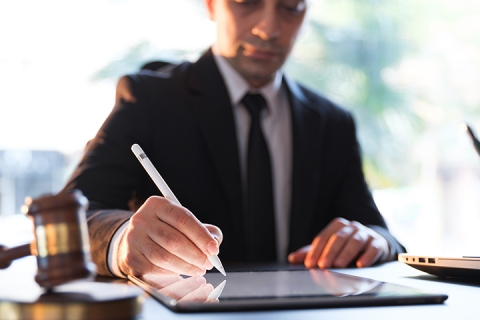 male office worker writing on his electronic tablet using a stylus, with a gavel beside him on the table
