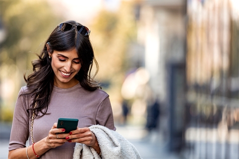 woman walking on the street outside smiling and using her phone