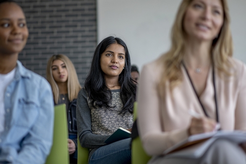 femme assise dans un public rempli de professionnels écoutant un orateur