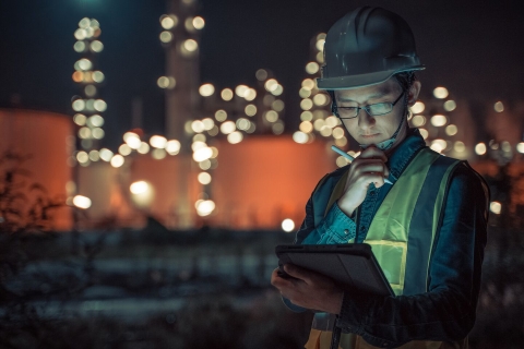 Petrochemical energy worker wearing hard-hat and using Smart tablet to communicate