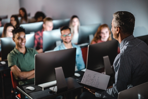 Teacher teaching in front of a group of students with laptops open