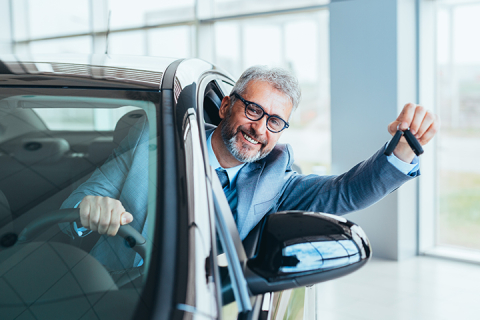 businessman sitting in car and showing car keys in car dealership showroom