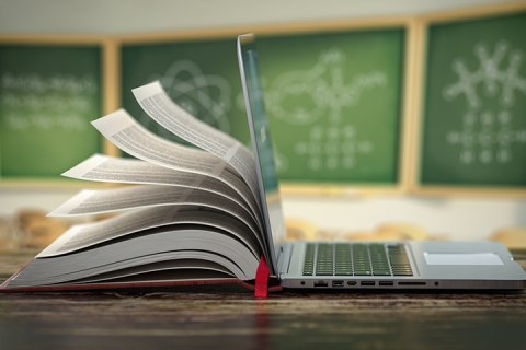 Book coming out of laptop in front of chalkboard in a classroom