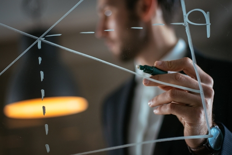 Homme dessinant un tableau de l'offre et de la demande sur un mur de verre