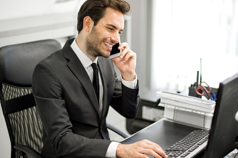 man working in his office and speaking on the phone with a smile on his face