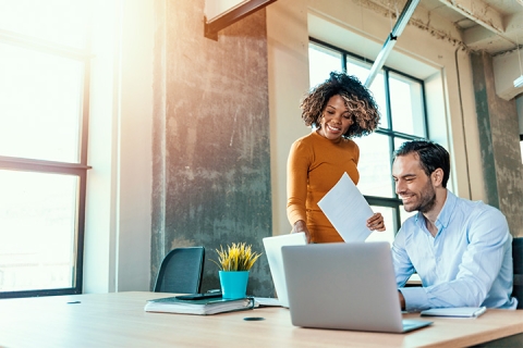 2 employees smiling, working together, and pointing at the computer screen