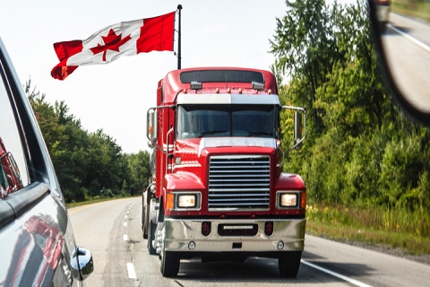 Tractor trailer driving down highway with Canadian flag flying