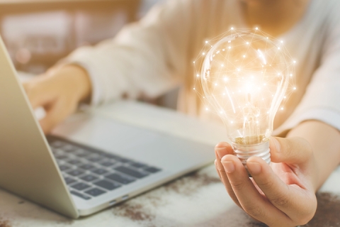 hand holding light bulb and using laptop on wooden desk