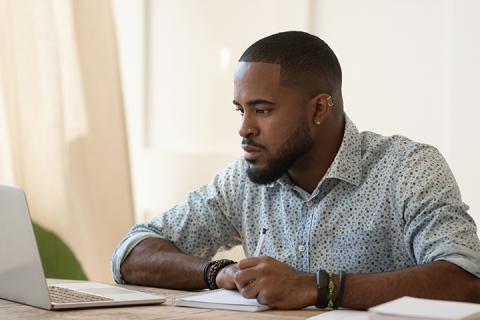 man sitting in front of a laptop and taking notes