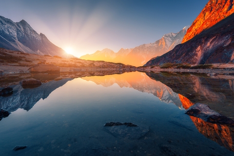 Beau paysage avec de hautes montagnes avec des pics illuminés, des pierres dans le lac de montagne, la réflexion, le ciel bleu et la lumière du soleil jaune au lever du soleil