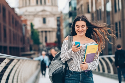 Smiling student walking and texting on the street
