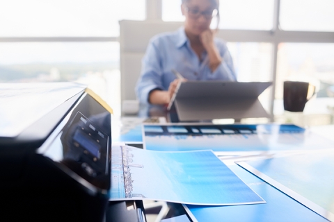 Woman working in an office and close-up of printer printing picture on paper