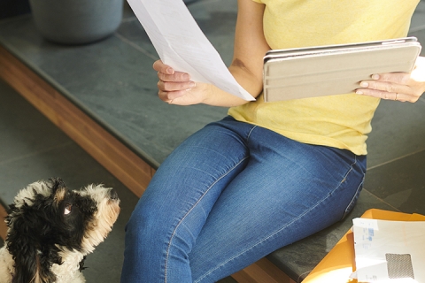 femme assise sur un sofa avec sa tabllette dans mains, son chien la regarde