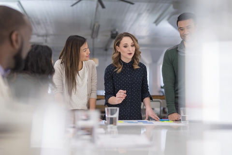 young CEO speaks to her team around a table in a open-space office