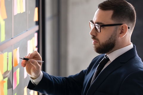 Mann mit Brille vor einer Pinnwand mit vielen Zetteln