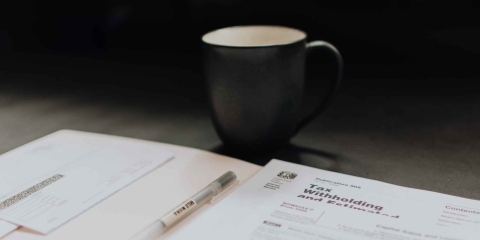 cup of coffee on a desk next to an open book with a pen inside