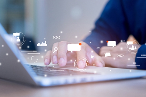 Digital message icons hovering above laptop keyboard being used by person