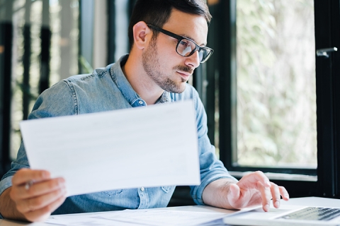 young businessman in office looking at and working with laptop, papers and documents