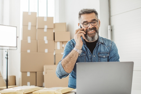 Homme avec barbe et lunettes au téléphone devant une pile de boîtes