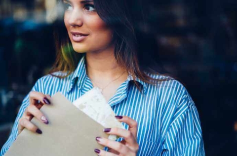 a brunette woman wearing a blue striped shirt holding a package and looking into the distance