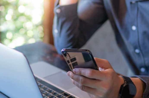 a man holding a black iPhone in front of his laptop