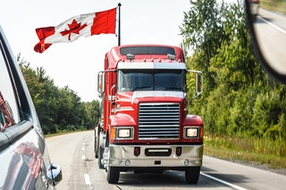 Tractor trailer driving on the highway with a Canadian flag flying