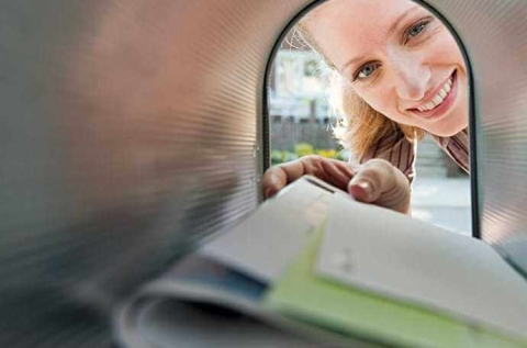 a woman peaking through a mailbox reaching for letters