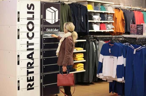 a blond woman collecting a parcel from a parcel locker located in a clothes shop