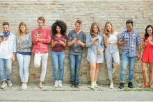 Diverse group of 9 young people standing next to each other against a limestone brick wall using smartphones