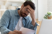 Frustrated man wearing glasses looking at paper invoice