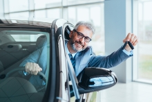 businessman sitting in car and showing car keys in car dealership showroom