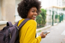 Portrait de derrière d'une femme afro-américaine en train de rire avec un sac et un téléphone portable marchant dans la rue de la ville
