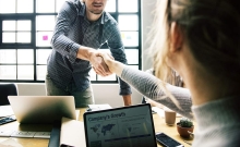 Two co-workers sitting across a table from each other shaking hands