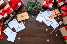  decorated wooden table with post mail letters envelopes and gifts boxes, presents with red ribbons. Xmas Santa office desk workplace background concept. Top view from above, flat lay.